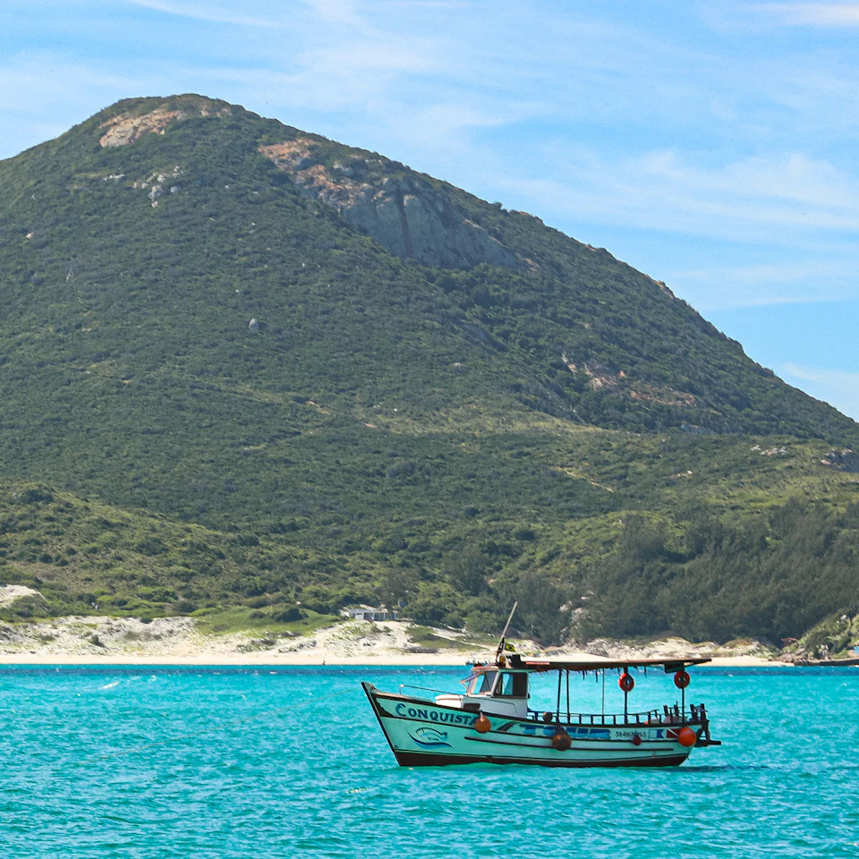 Barco de passeio em mar azul-turquesa diante de um morro coberto de vegetação